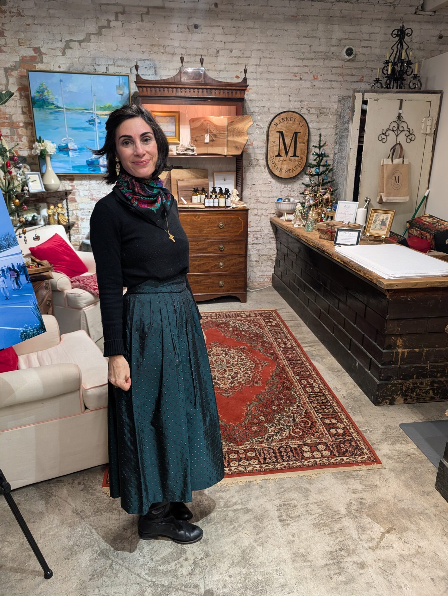 Woman standing in a decorated room with furniture, artwork, and a patterned rug.