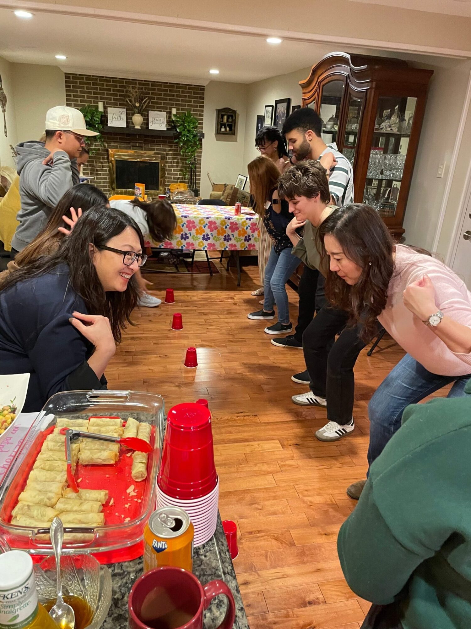 People gathered around a table with a red and white cake, in a room with wooden floors and a brick wall.