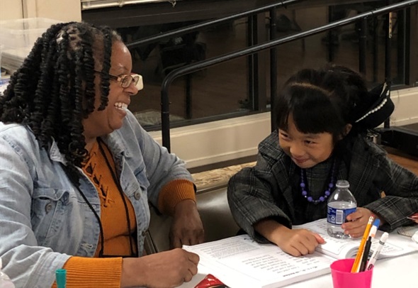 Two women sitting at a table, smiling and talking, with papers and a water bottle in front of them.