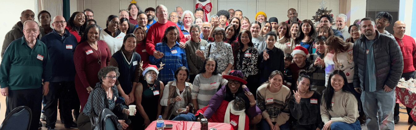 Large group of people gathered indoors, some smiling, some holding balloons, in a festive setting.