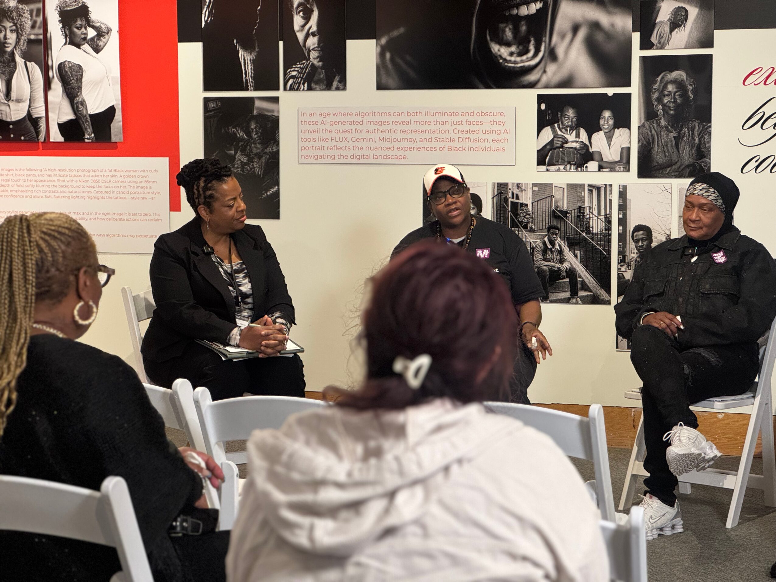 Three people seated in a panel discussion with a group of audience members in a room with black-and-white photos on the wall.