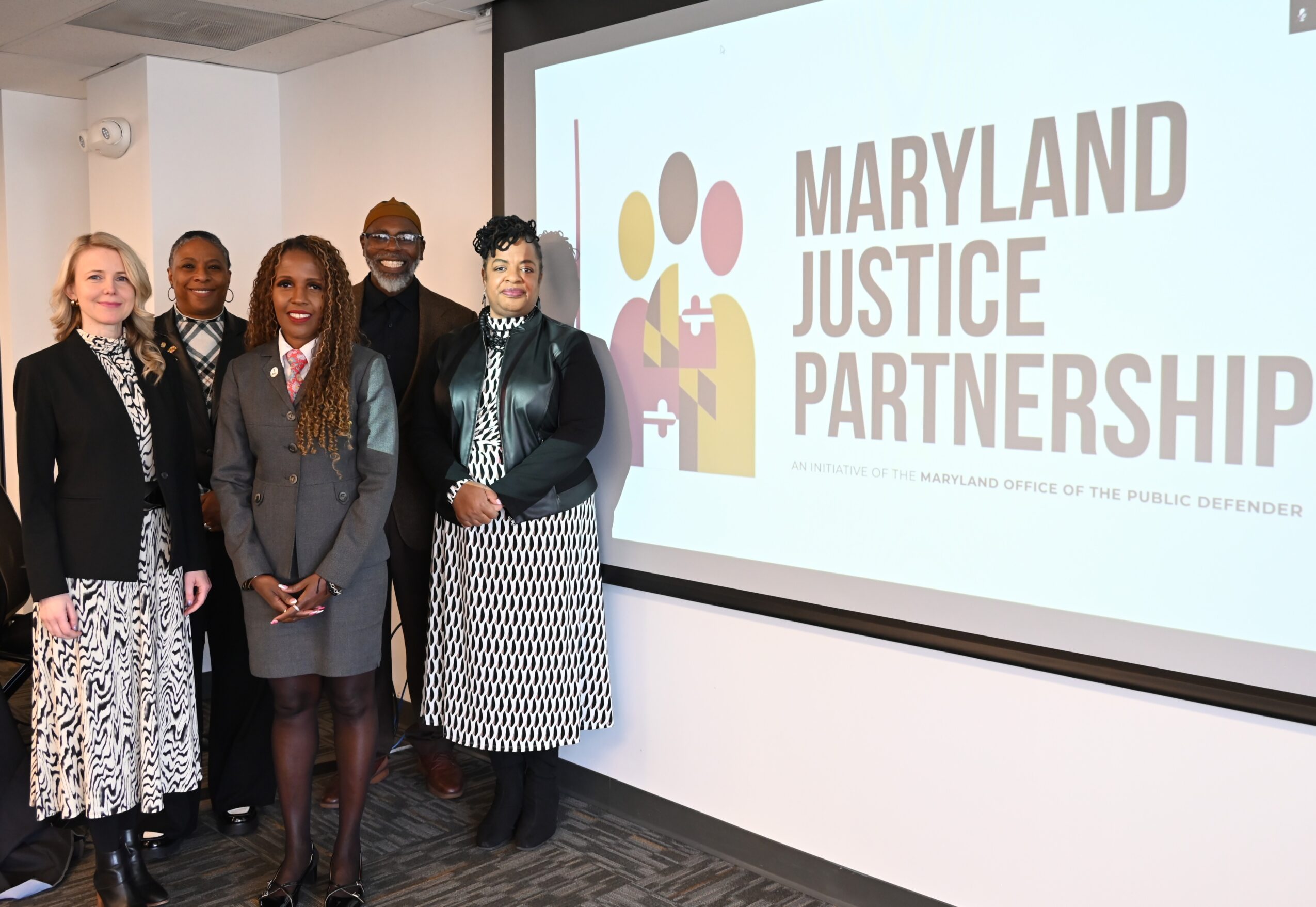 Five women standing in front of a screen displaying Maryland Justice Partnership logo in a conference room.