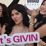 Three women smiling and posing, one holding a sign that says