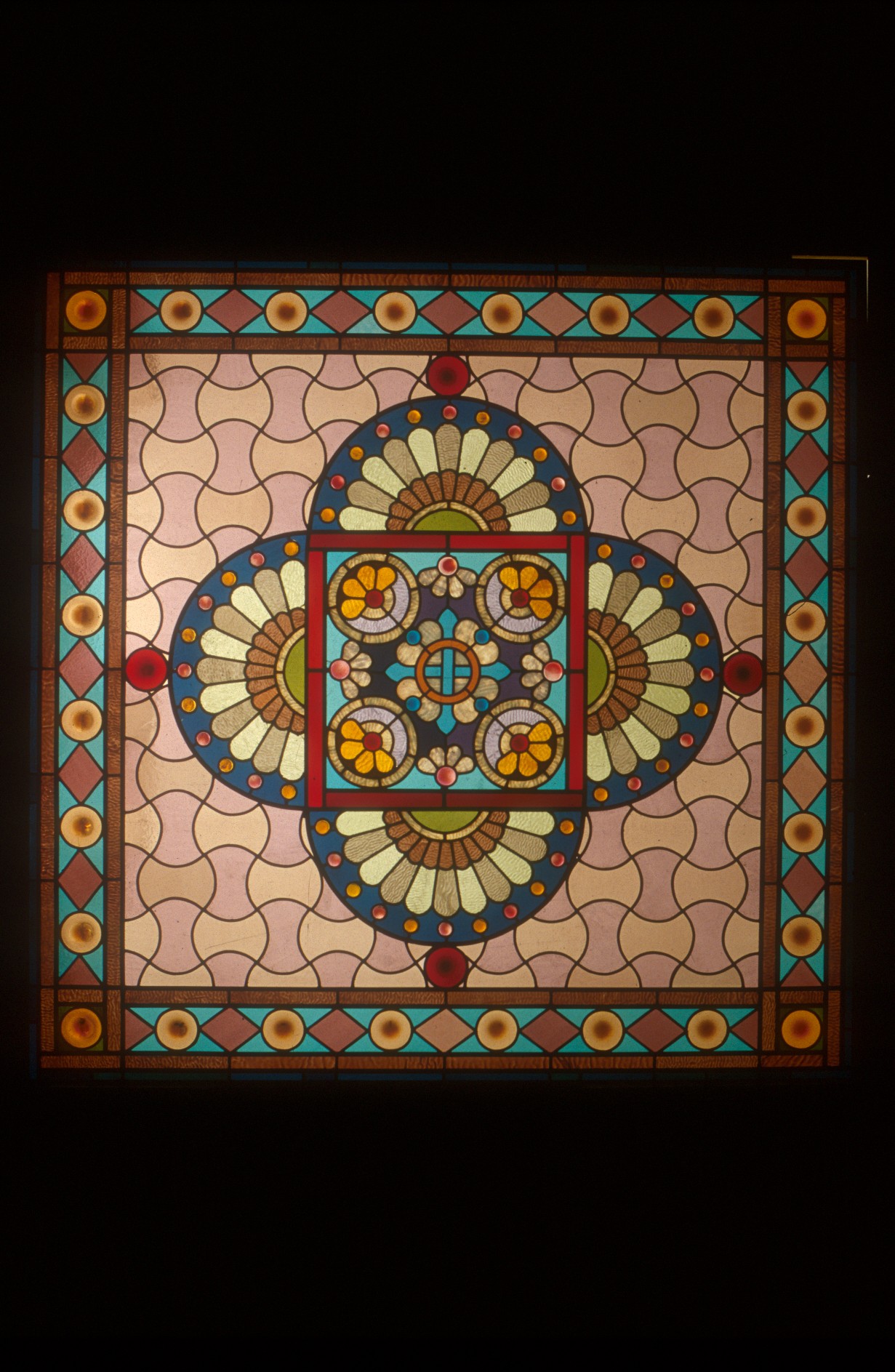 Colorful stained glass window with geometric patterns and floral motifs, framed by a decorative border.