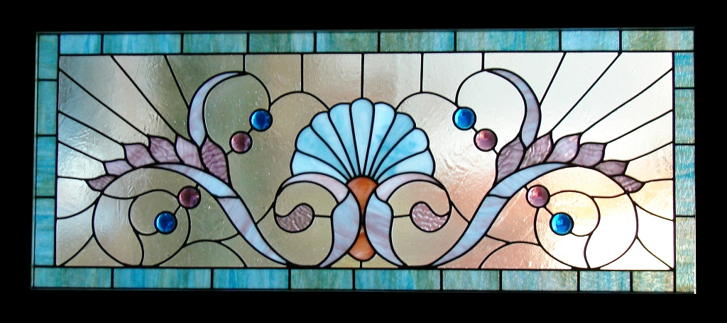 Colorful stained glass window with floral and scroll patterns, featuring a central shell motif, surrounded by geometric shapes.