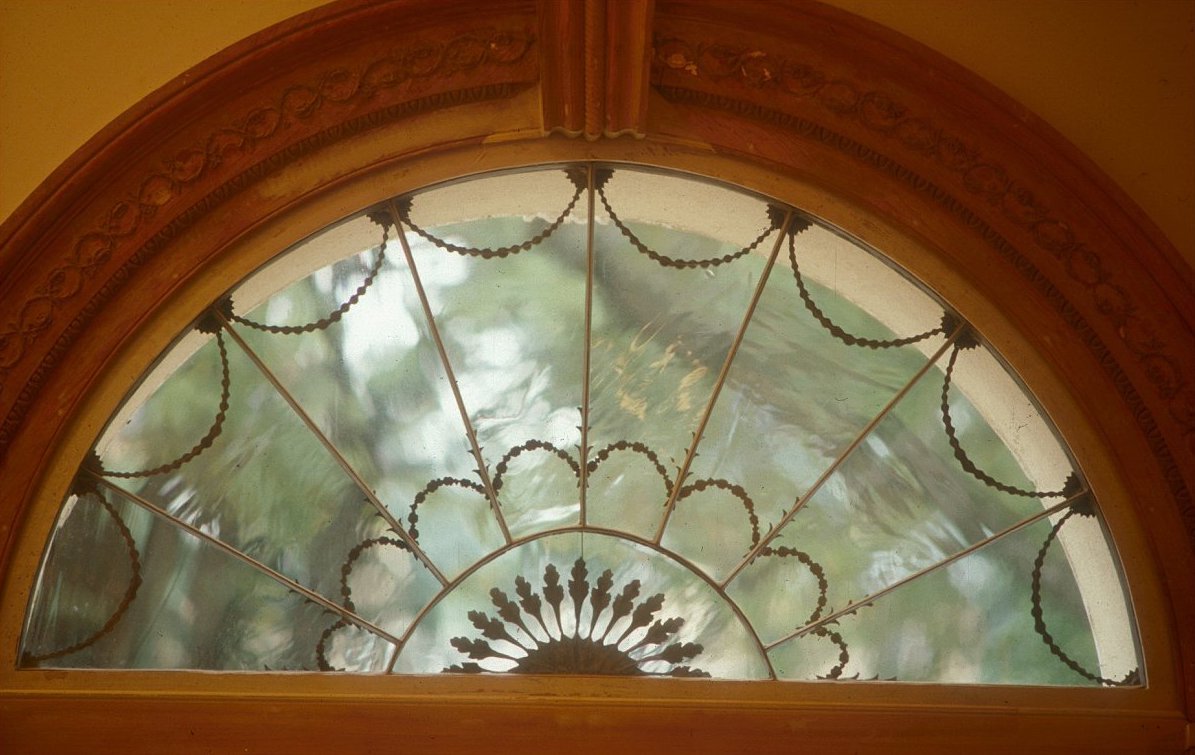 Decorative semi-circular window with a stained glass design and a view of trees outside.