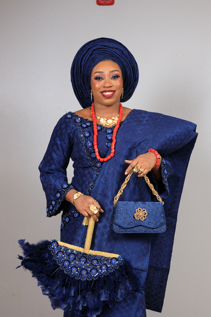 Woman in traditional blue attire holding a matching handbag and umbrella, smiling, against a plain background.