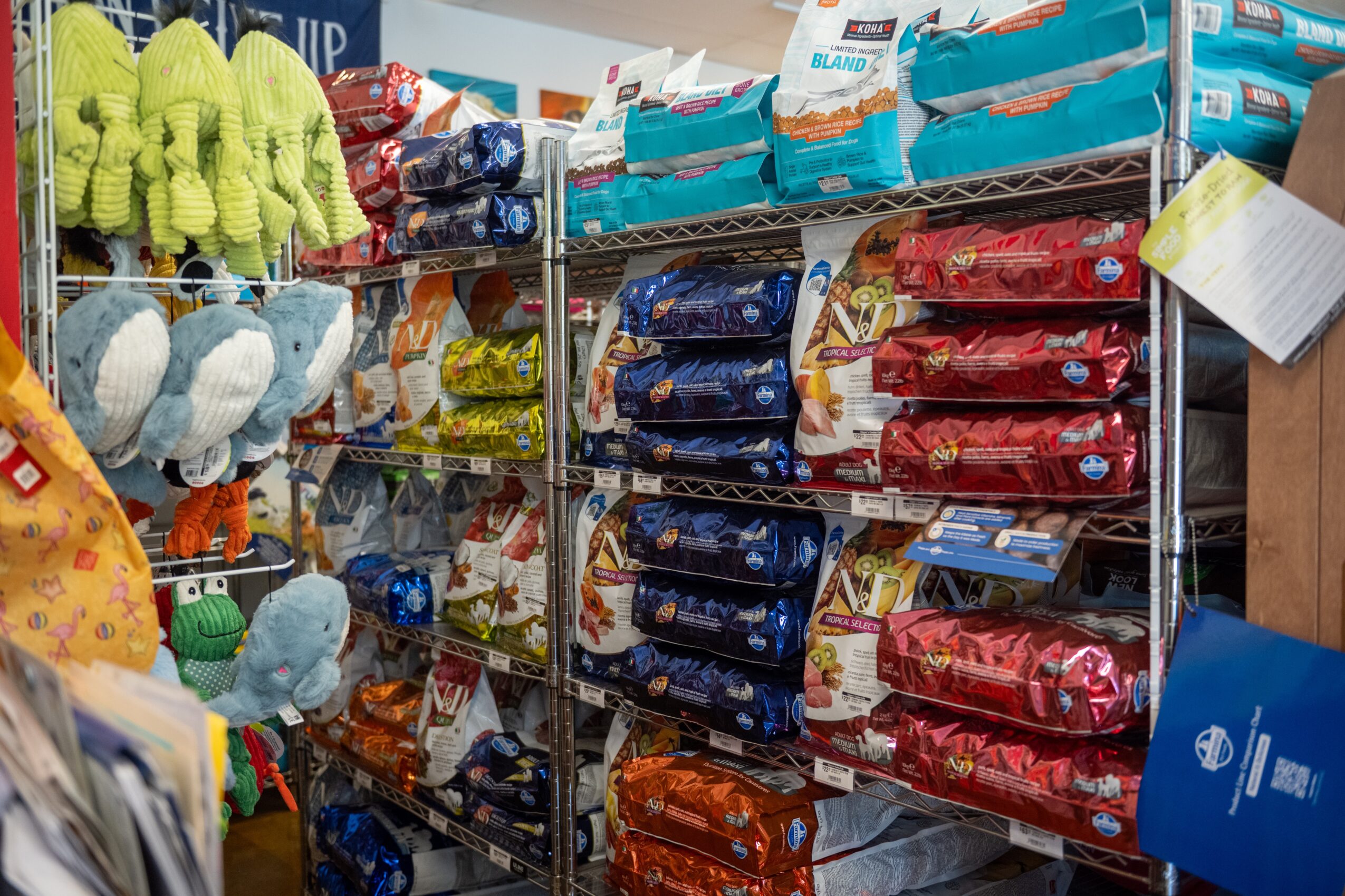 Shelves stocked with pet food bags and plush toys in a store, with colorful packaging and products.
