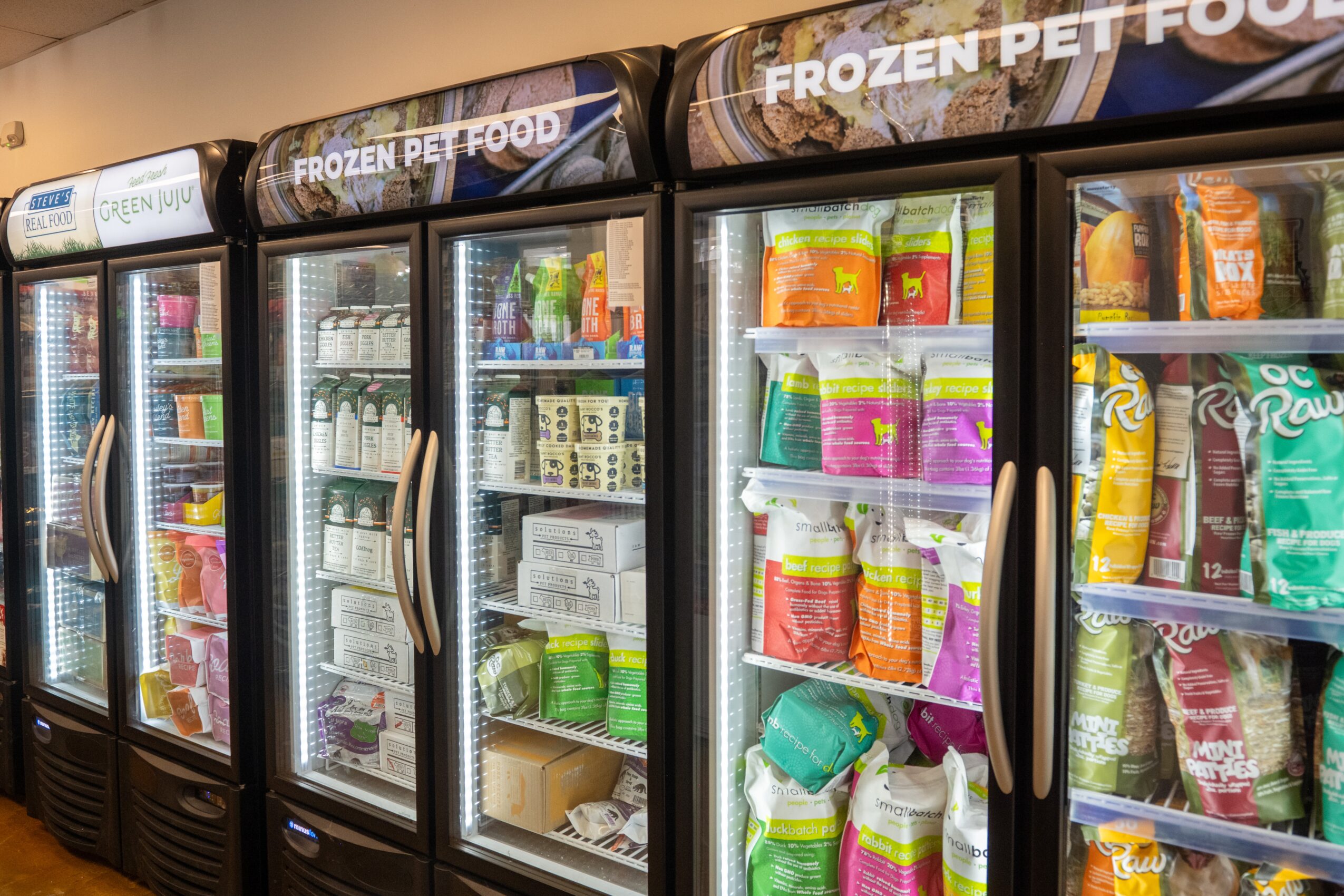 Frozen pet food freezer with glass doors filled with various pet food packages, in a store aisle.