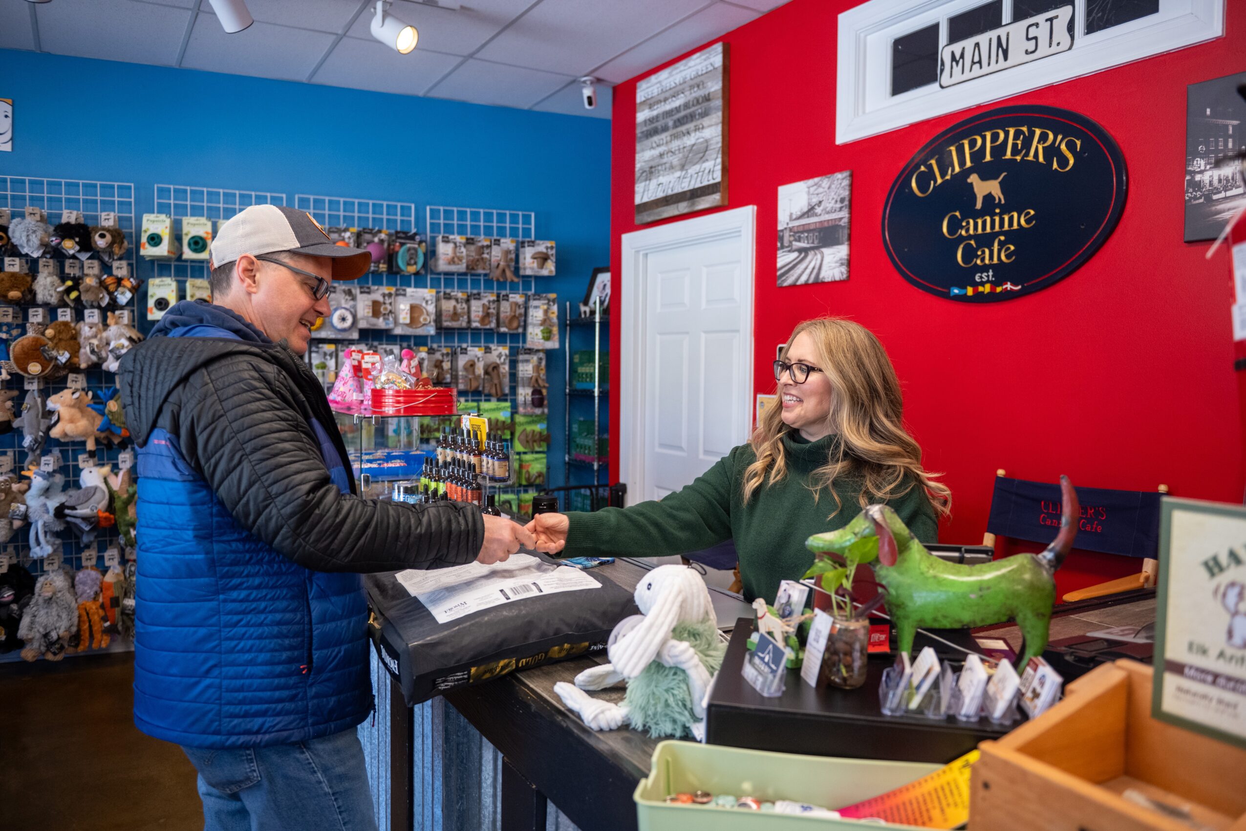 A man and woman shake hands inside a pet store, with shelves of pet supplies in the background.