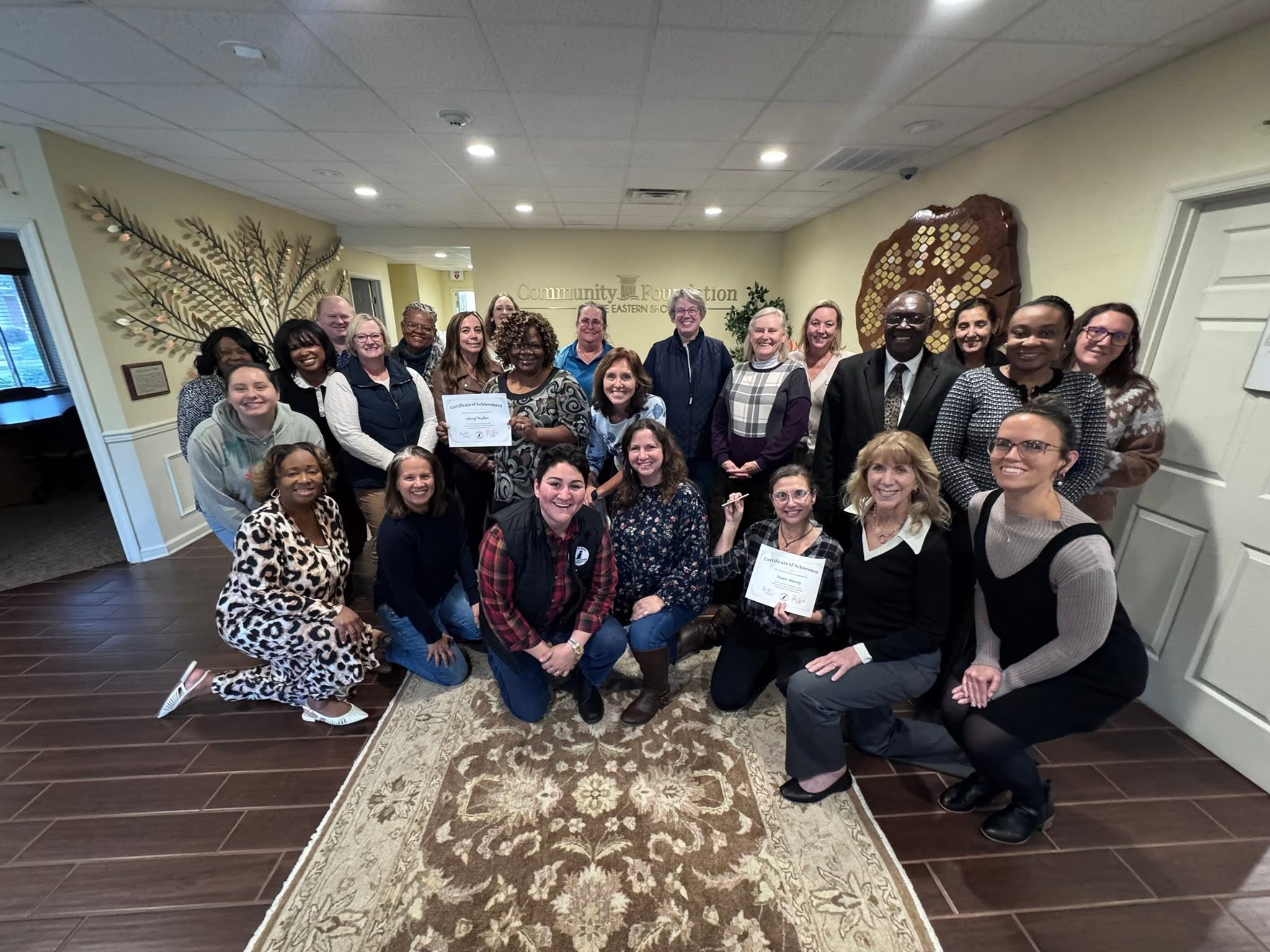 Group of people indoors, some holding certificates, posing for a photo in a decorated room.