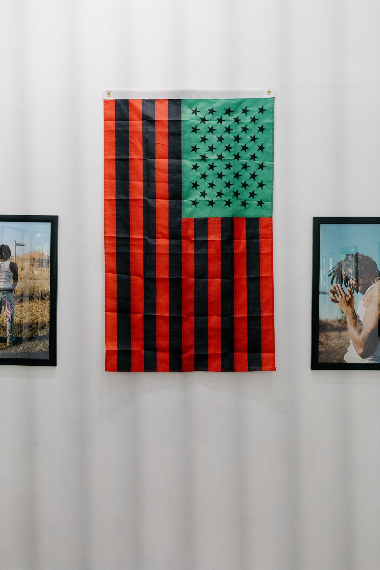 Flag with red and black stripes and a green section with black stars, hanging on a white wall.
