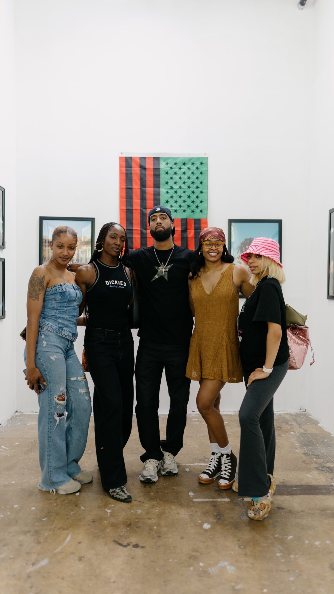 Group of five people standing together in an art gallery, smiling, with colorful artwork on the wall behind them.