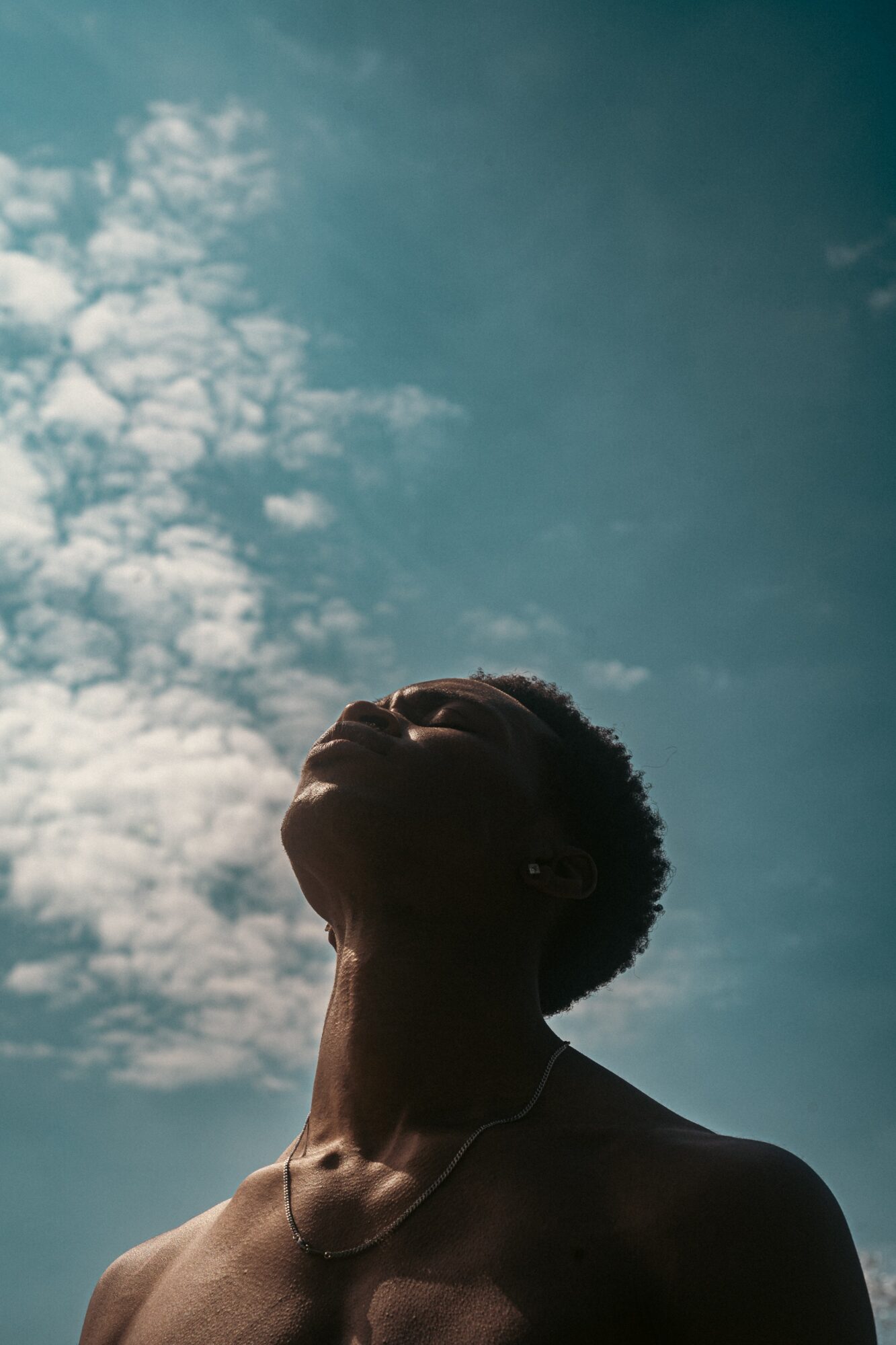 Silhouette of a person with short hair looking upward against a cloudy sky.