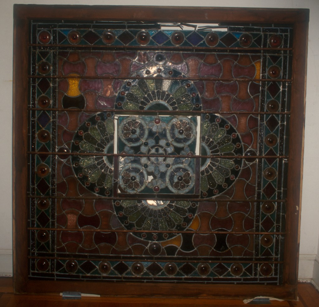 Decorative stained glass window with intricate patterns and colorful glass pieces, framed by wood, leaning against a wall.