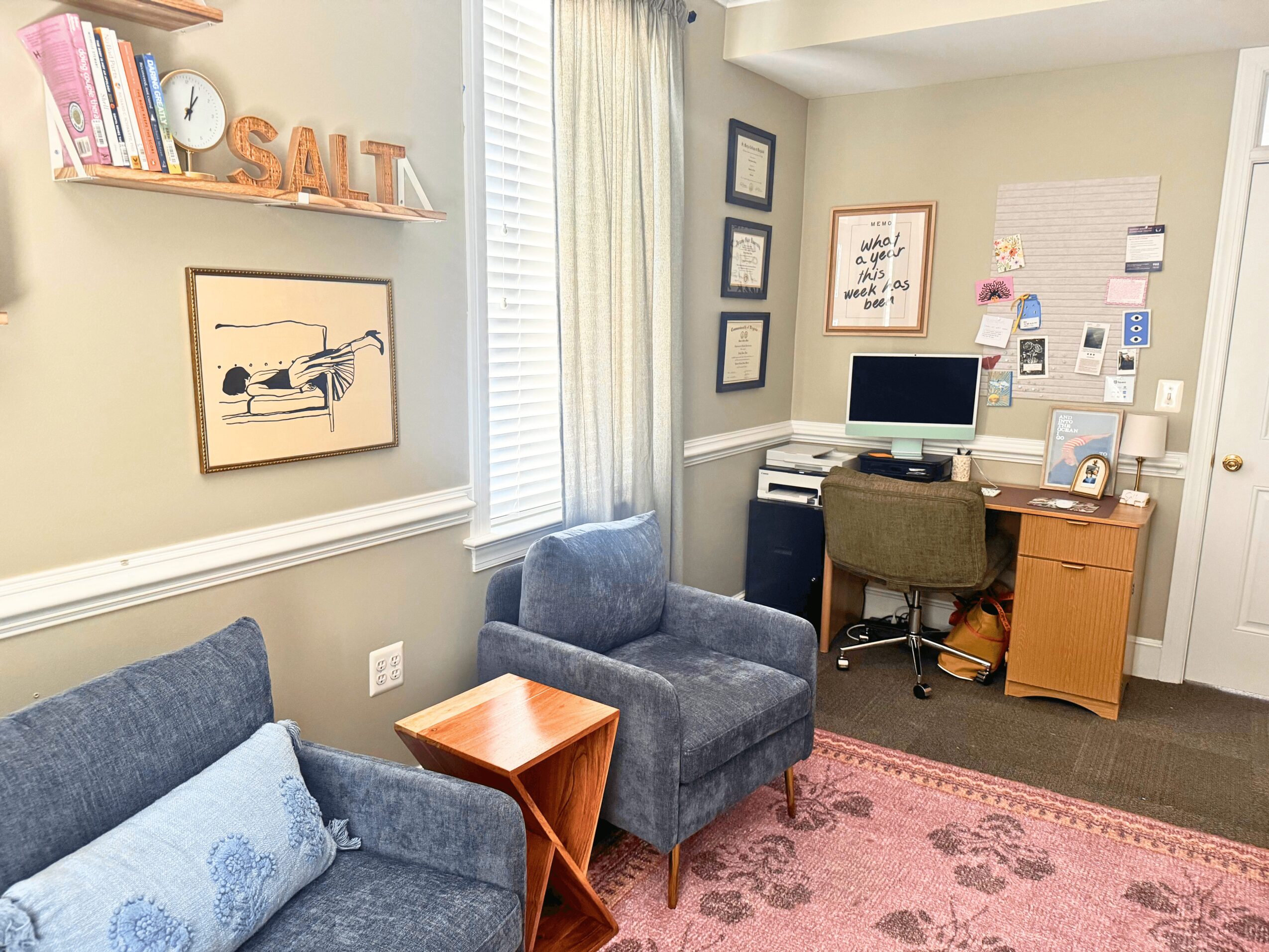 Home office with desk, computer, chair, armchair, sofa, bookshelf, and wall decorations, in a cozy room with natural light.