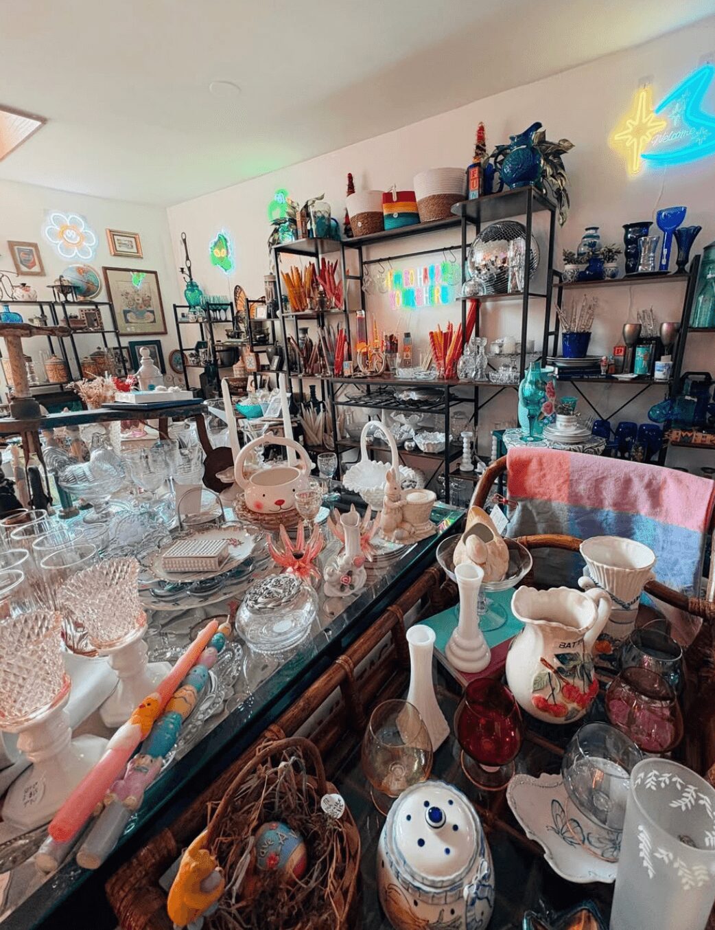 Room filled with shelves and tables displaying various glassware, ceramics, and decorative items in a bright, organized space.