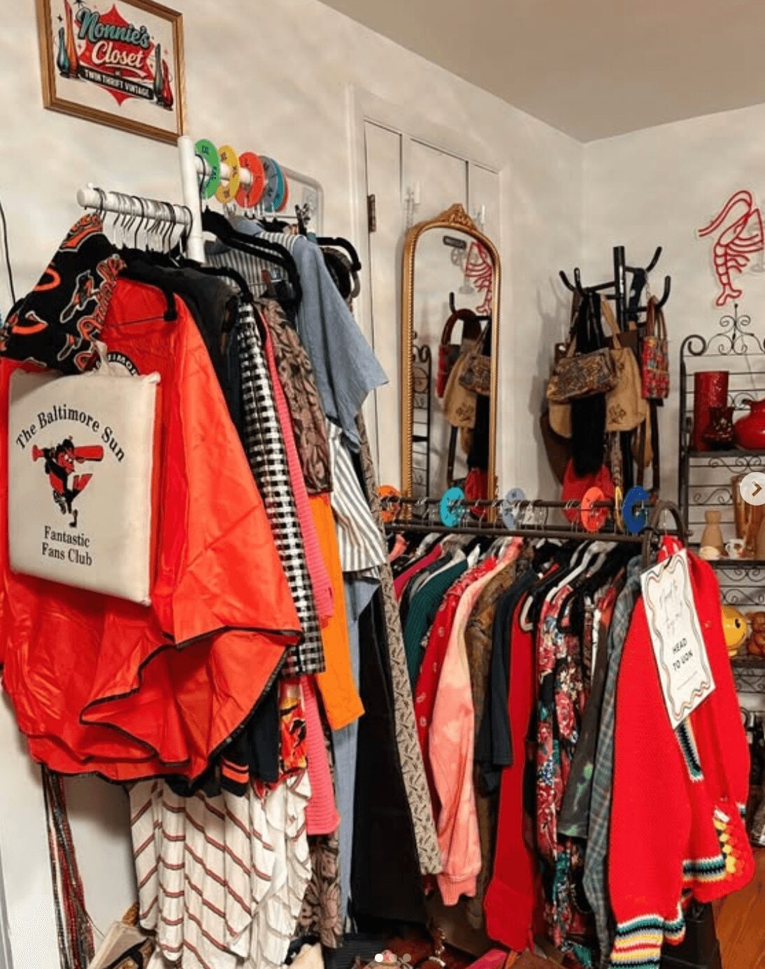 Clothing rack with various colorful garments, bags, and accessories in a boutique store, with a mirror and decorative items in the background.