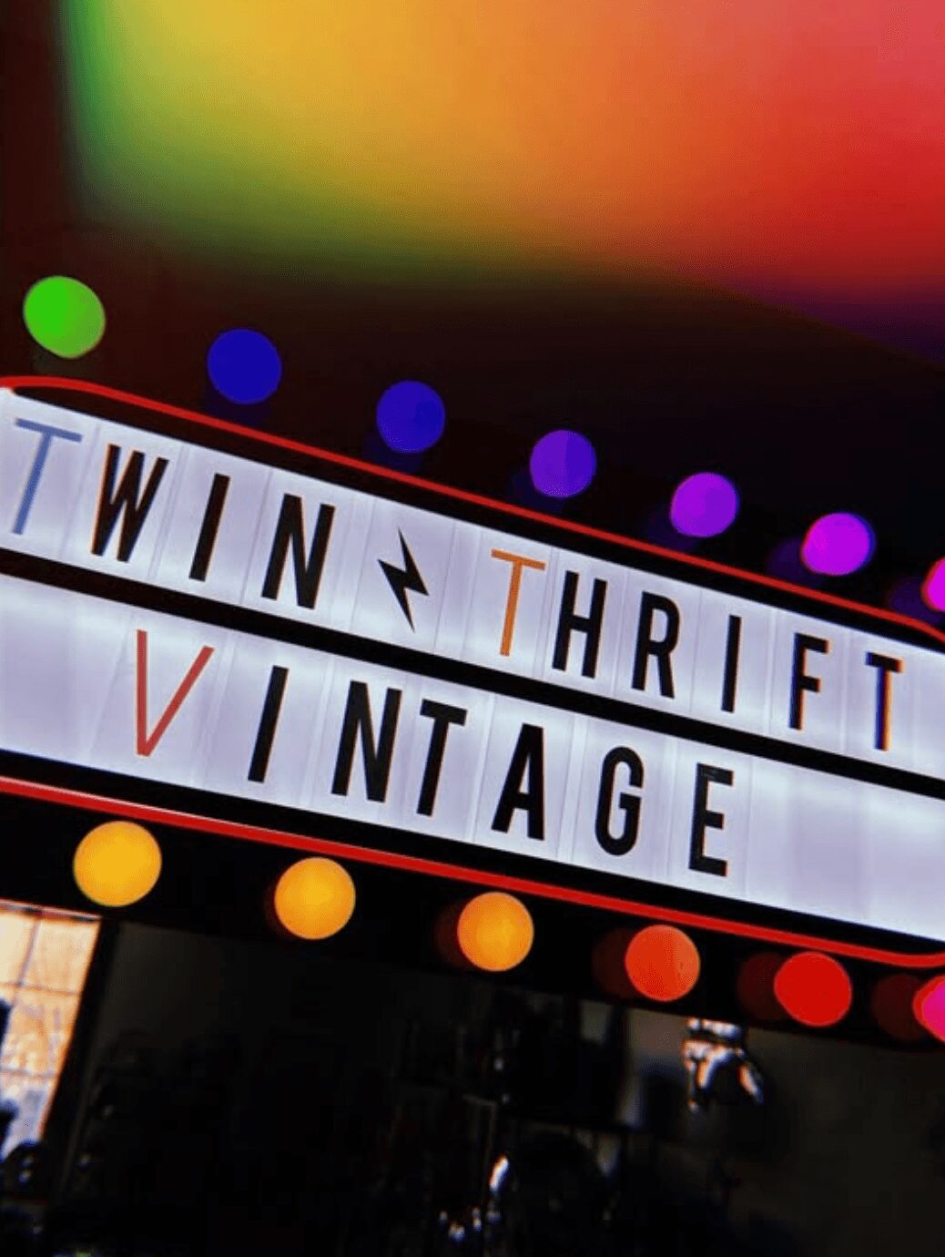 Sign with the words 'TWIN THRIFT VINTAGE' and colorful lights above and below, on a dark background.