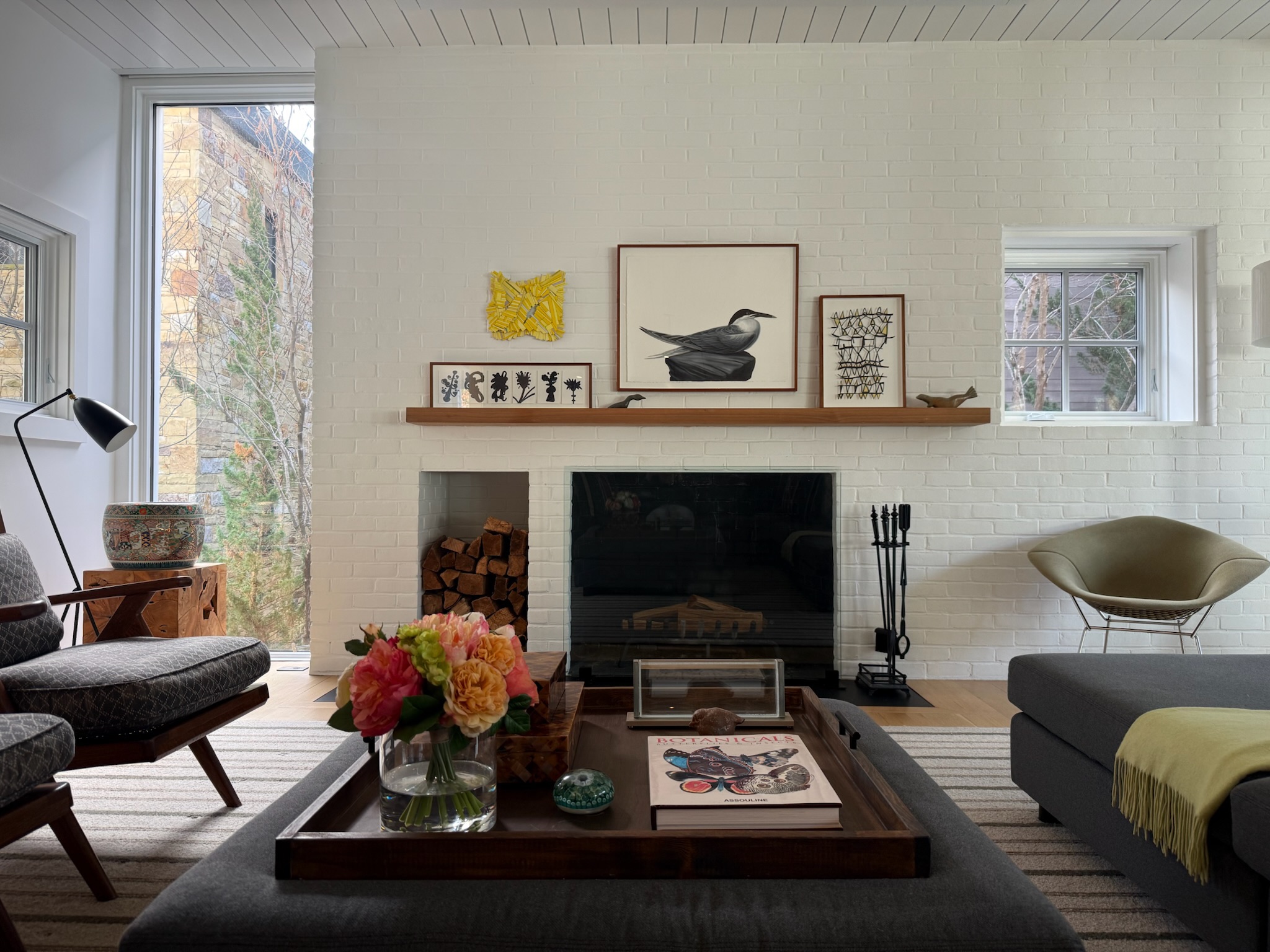 Living room with fireplace, artwork, window, and furniture including a coffee table with flowers and a sofa.