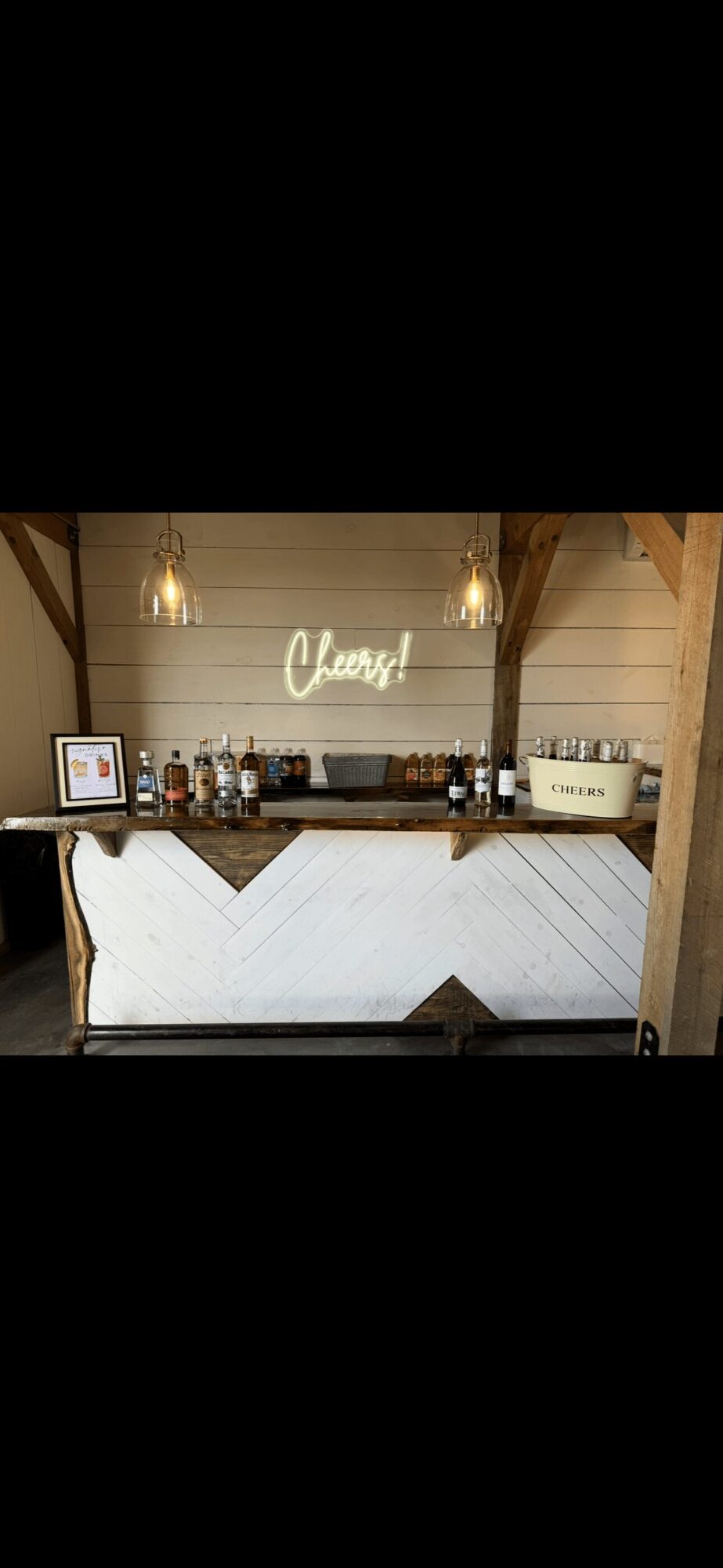 Bar area with bottles, a neon sign, and a white counter, in a wooden setting, with warm lighting.