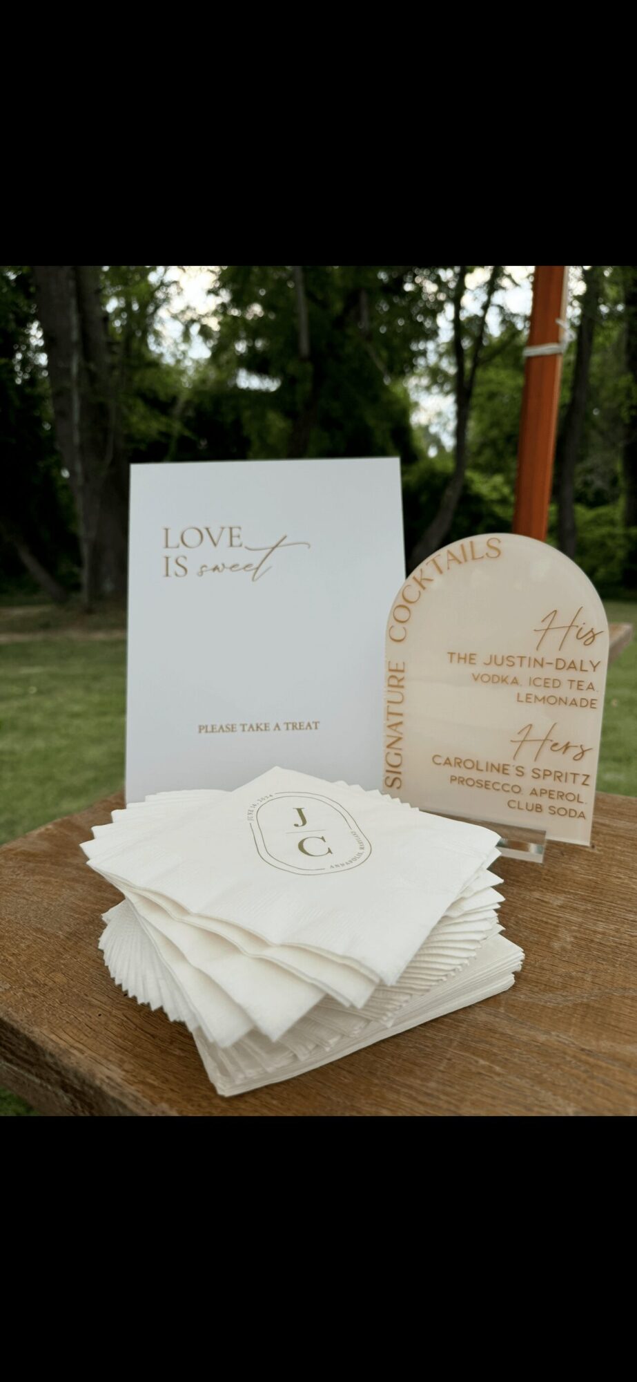 Stack of white napkins with a small card and a semi-circular card behind them outdoors, trees in background.