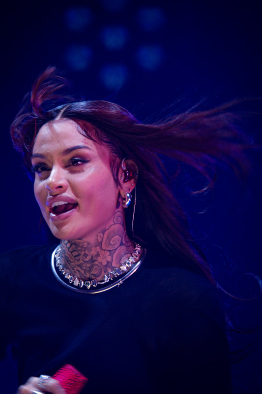 Woman with long hair flowing, wearing jewelry, smiling, against a dark background with blue lights.