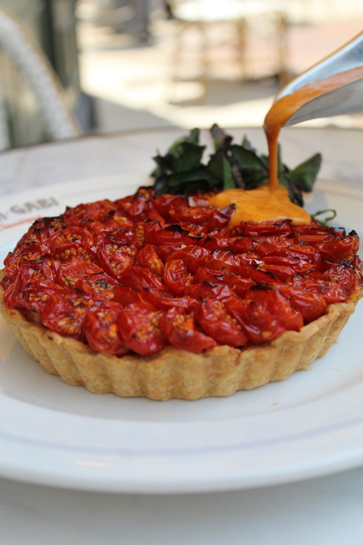 Cherry tomato tart with a golden crust, topped with cherry tomatoes, and garnished with greens, with sauce being poured on top.