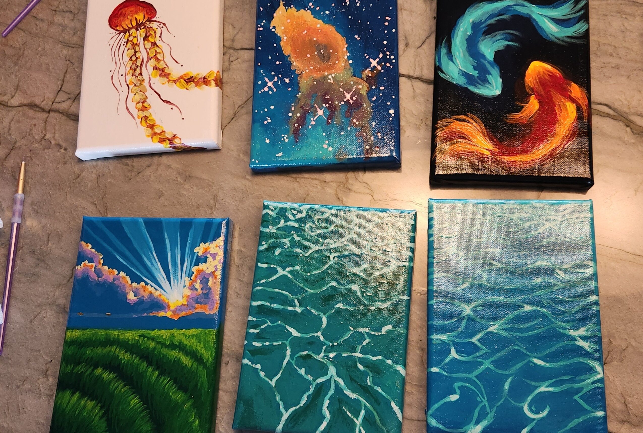 Six colorful abstract paintings of various natural and fantastical scenes arranged on a surface.