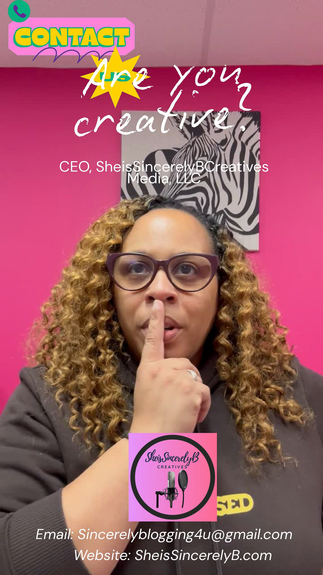 Woman with glasses and curly hair holding finger to lips in front of pink wall with motivational quote and logo