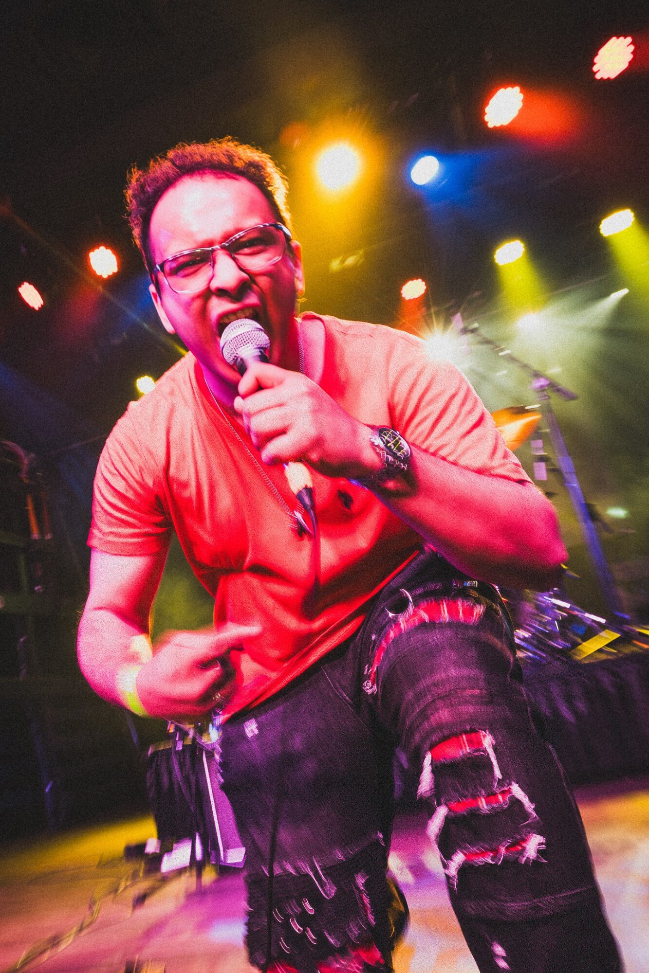 Person singing into a microphone on stage with colorful lights in the background