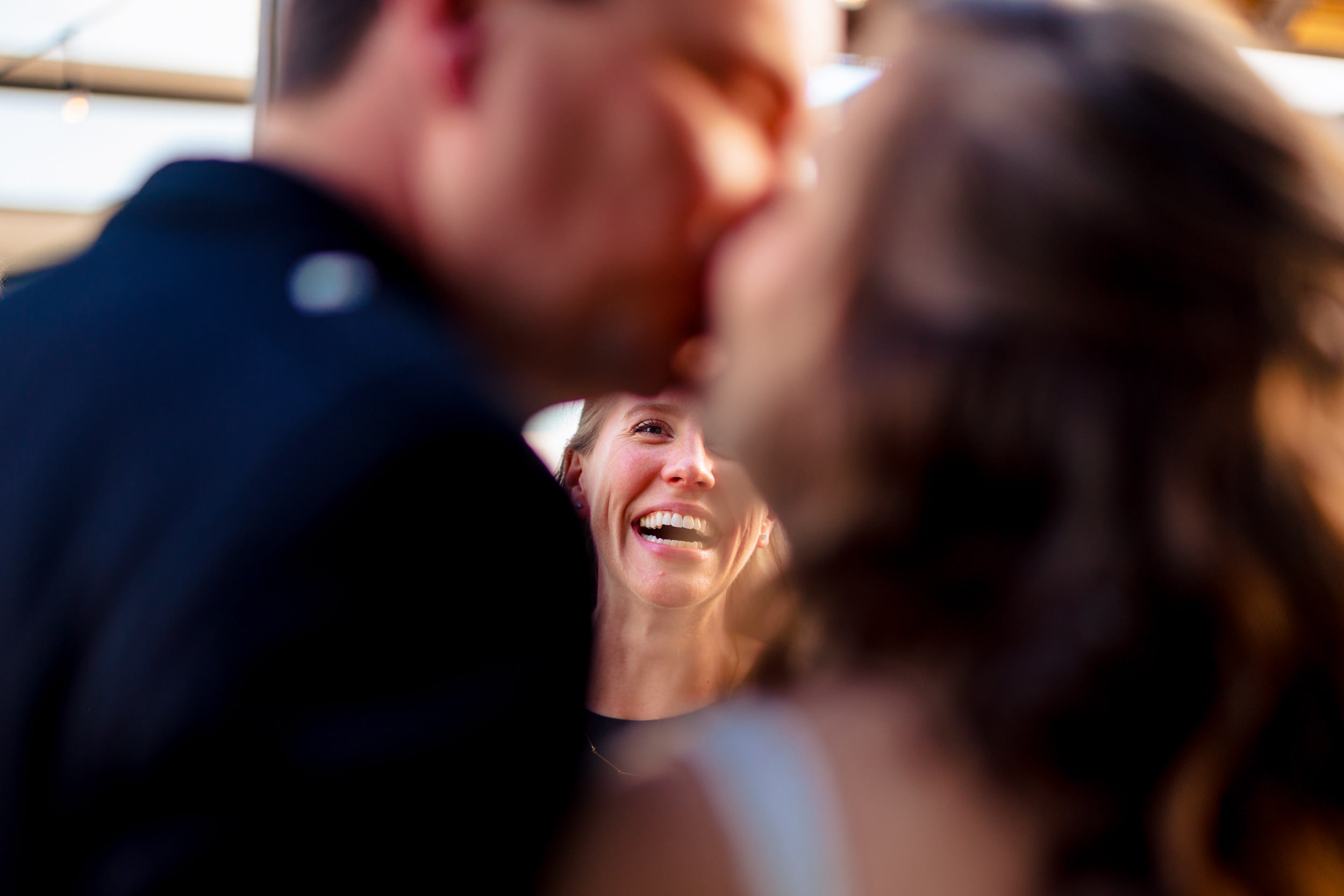 Three people are close together, with one person smiling in the background, partially obscured by the other two in the foreground.