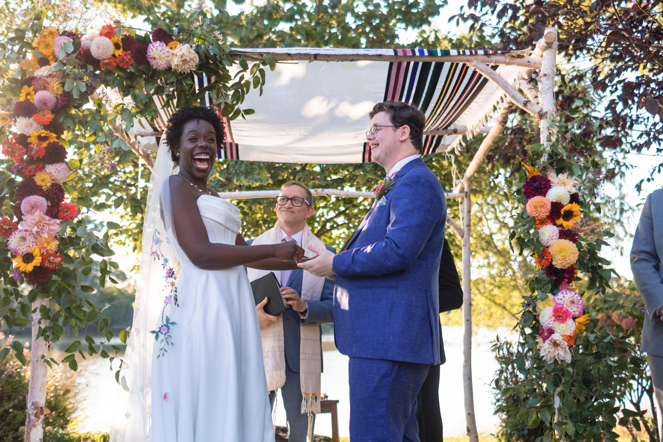 A wedding ceremony with a bride and groom holding hands, surrounded by floral decorations and an outdoor setting.