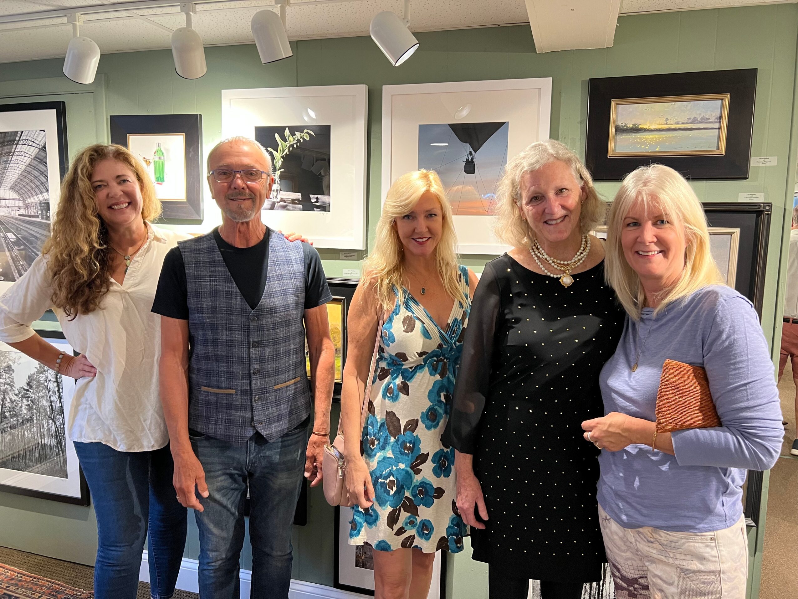 Group of five people smiling in an art gallery, standing in front of framed artwork on a green wall.