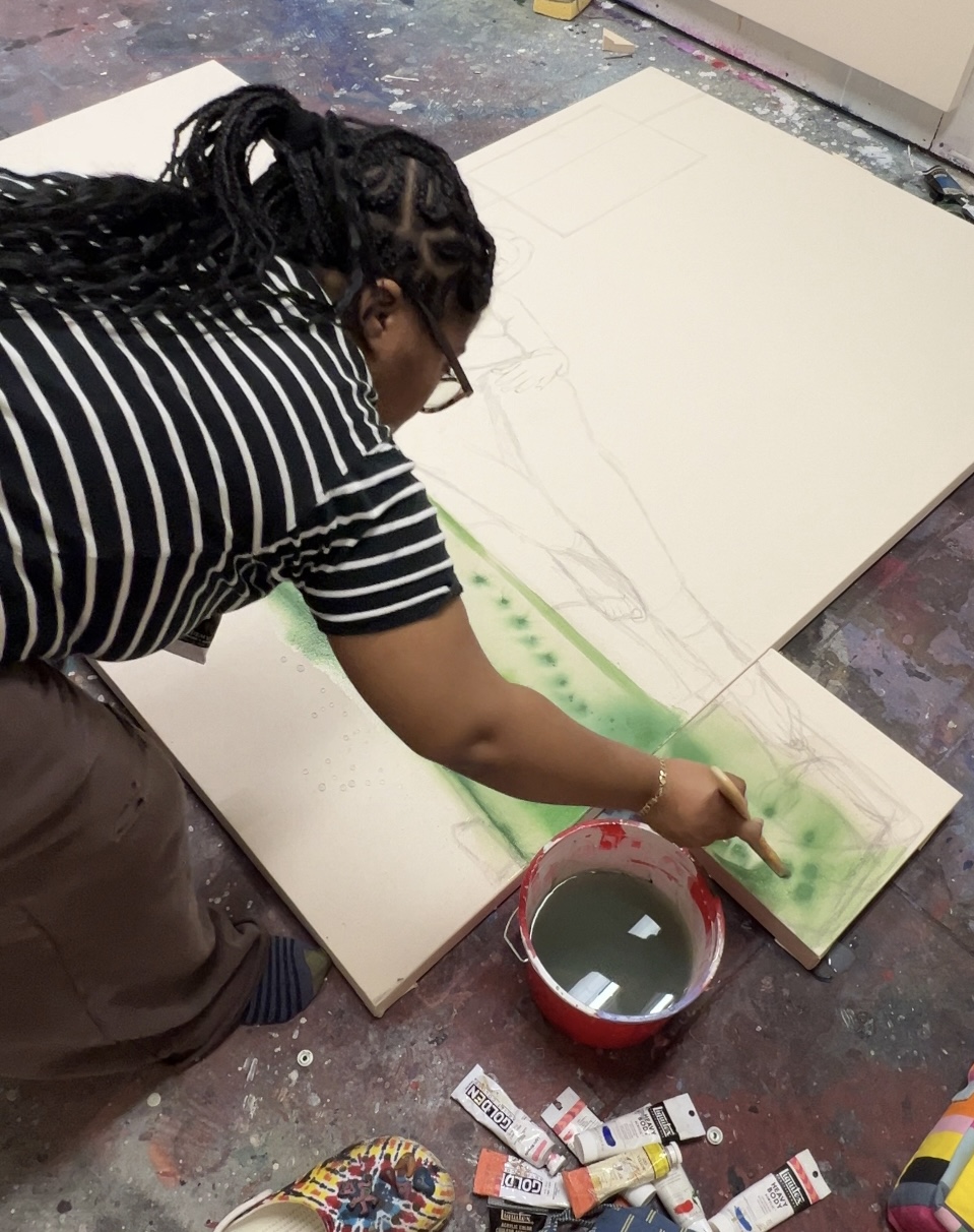 Person painting on large canvas with green paint, surrounded by art supplies, in an art studio.