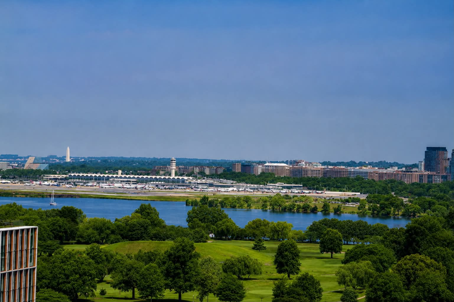 Landscape view of a river, green trees, and a city skyline with buildings and a bridge in the distance.