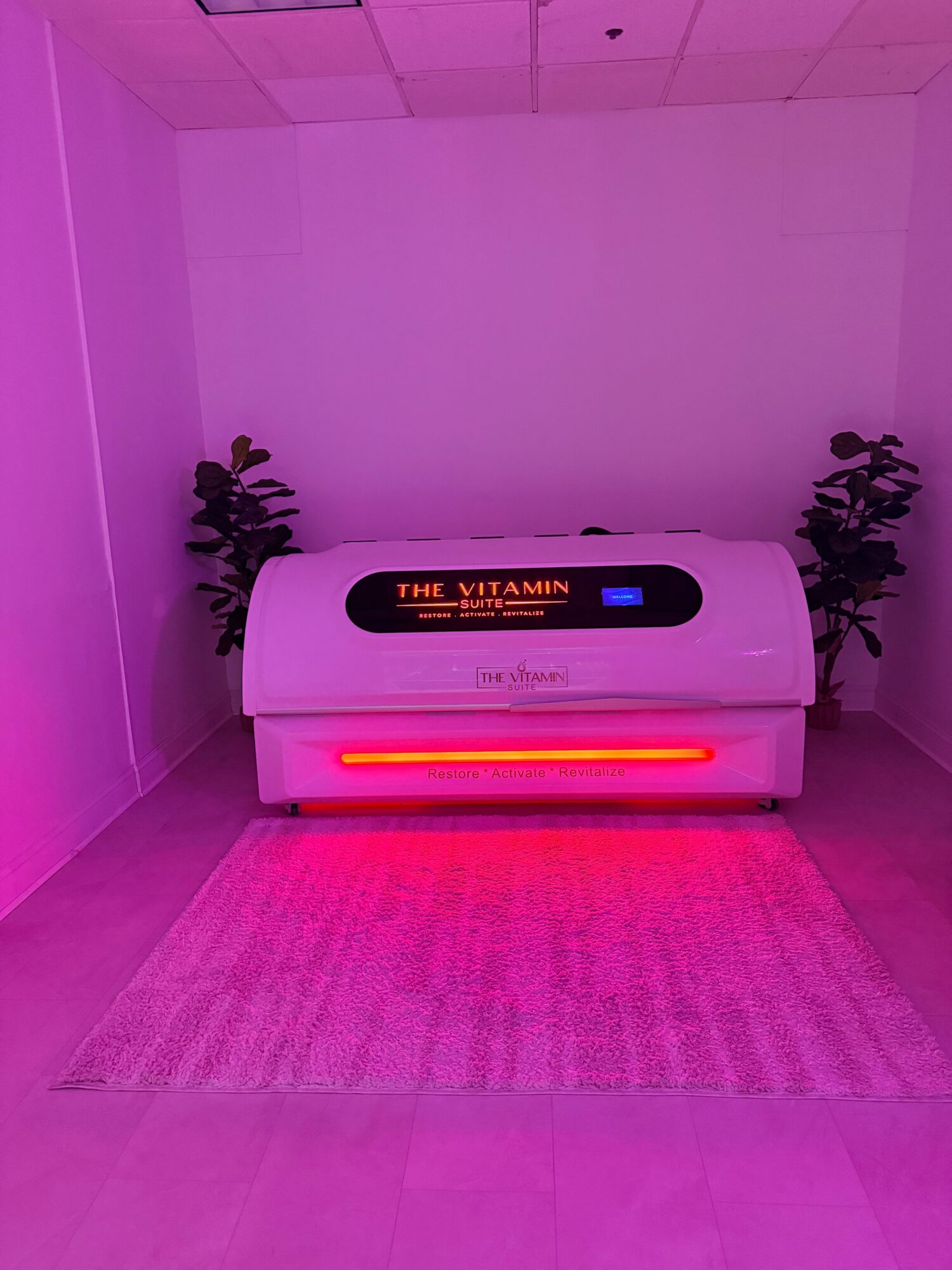 Air purifier with digital display and red light, placed on a pink rug in a room corner, with plants nearby.