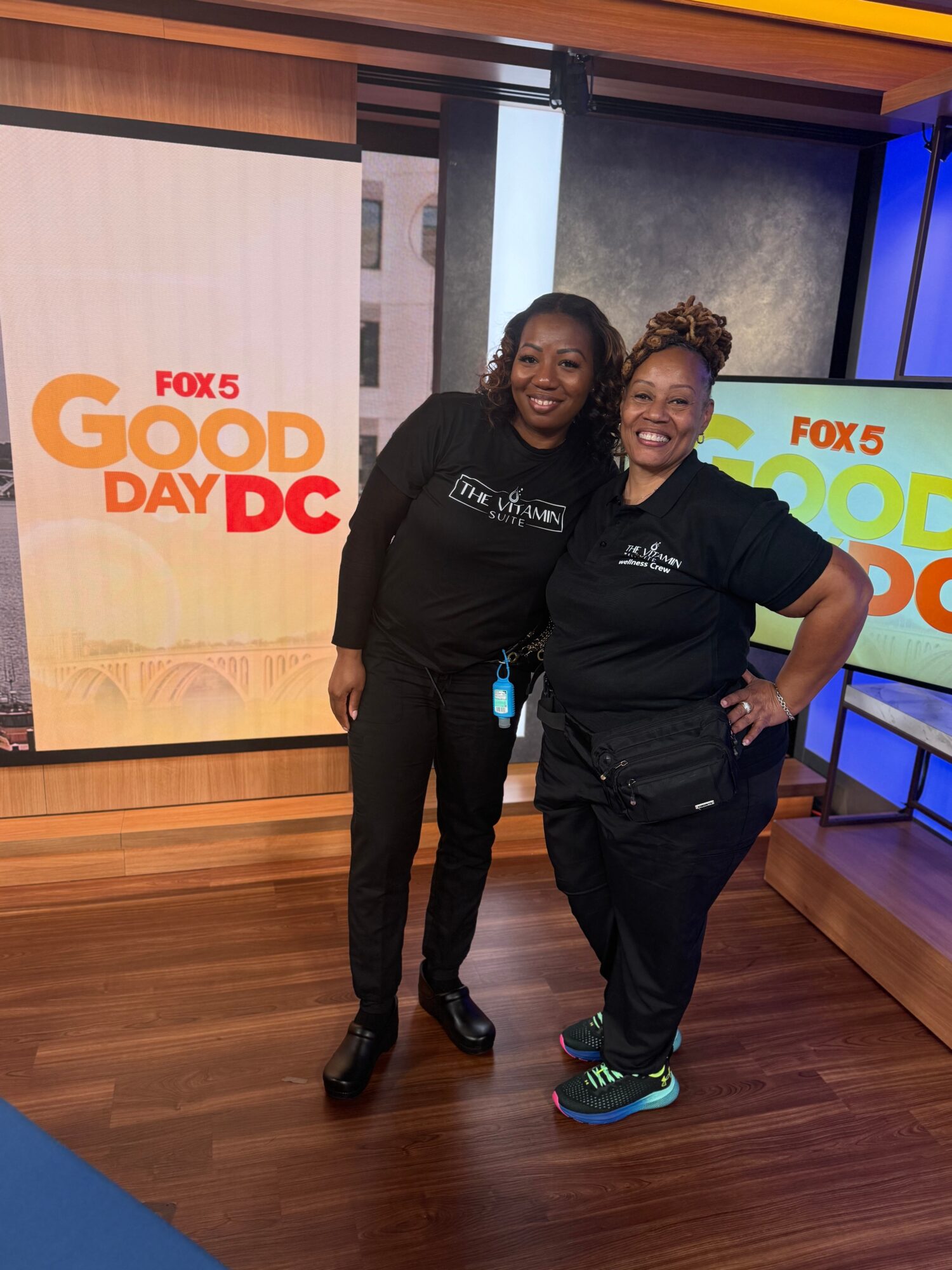 Two women stand together smiling in a TV studio with FOX 5 Good Day DC screens behind them.