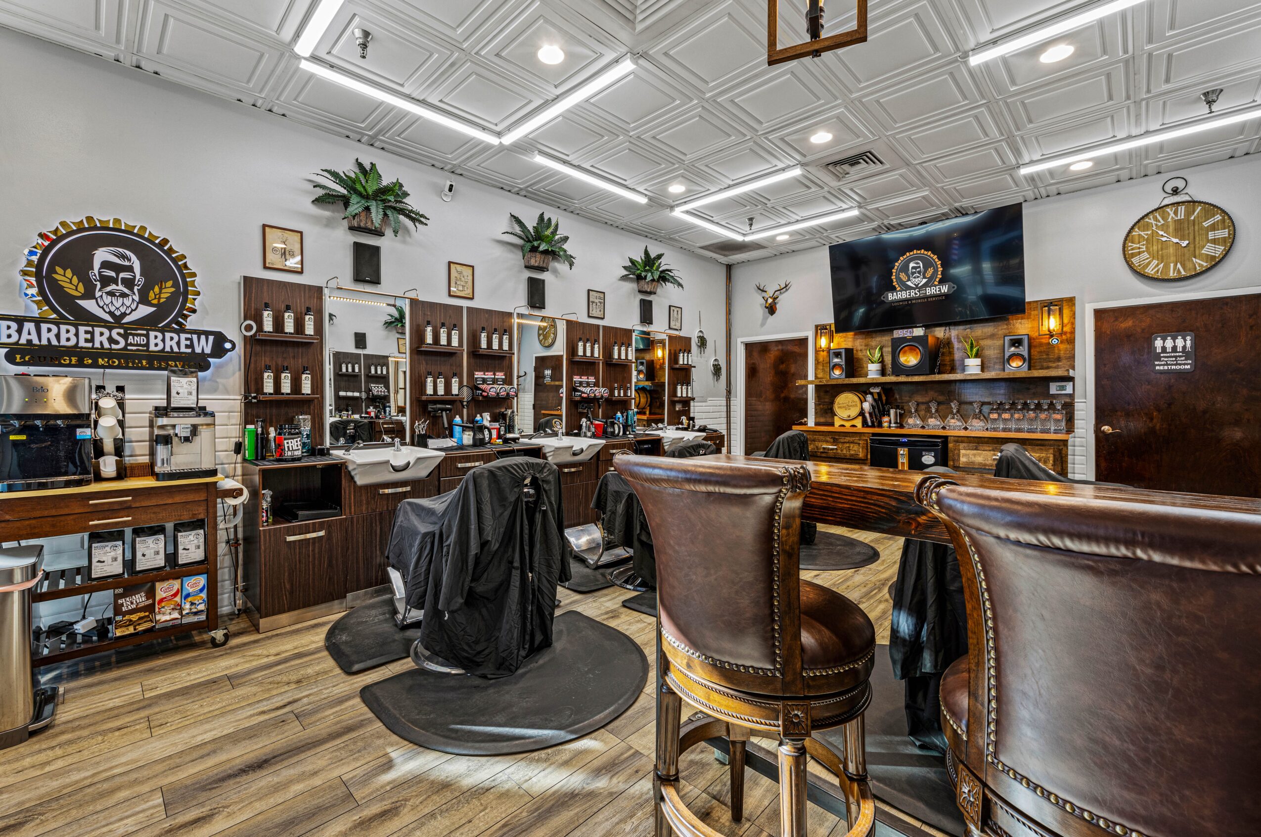 Barbershop interior with chairs, shelves, and a television, featuring wooden furniture and decorative plants.
