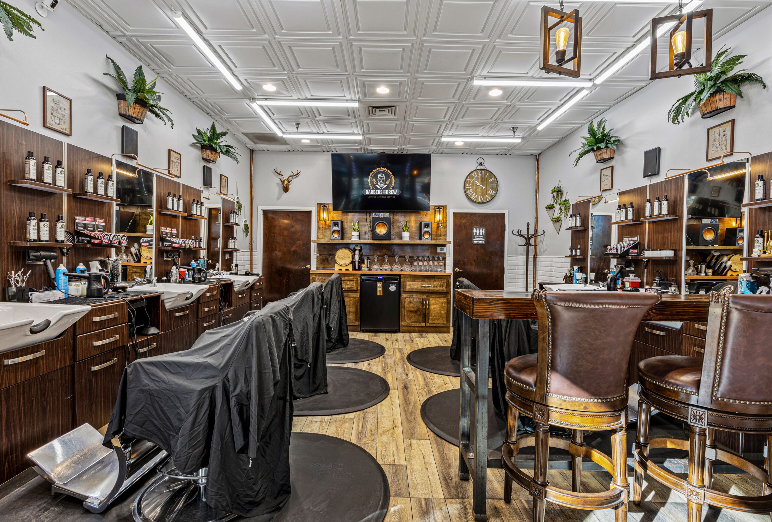 Elegant bar with wooden shelves, plants, and seating area, illuminated ceiling lights, and a large TV on the wall.