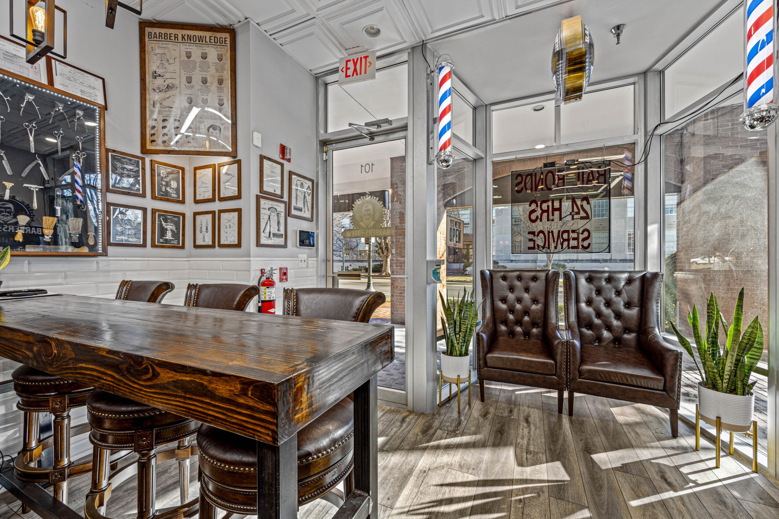 Interior of a cafe with a wooden table, leather chairs, framed pictures on the wall, and large windows with barber pole decorations.
