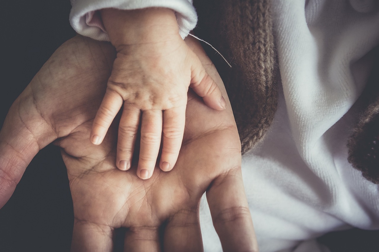 Close-up of a small child's hand resting on an adult's hand, both hands visible in the image.