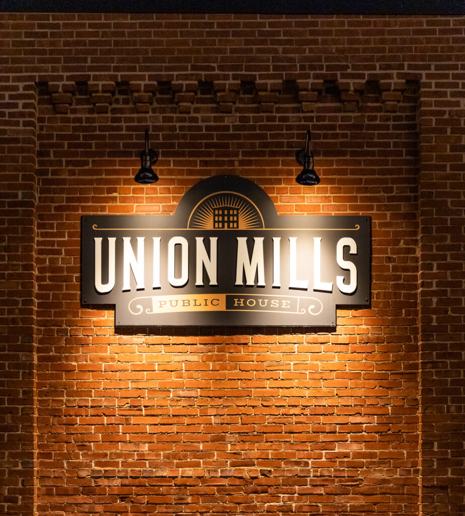 Brick wall with illuminated sign reading 'Union Mills Public House' and a logo above.
