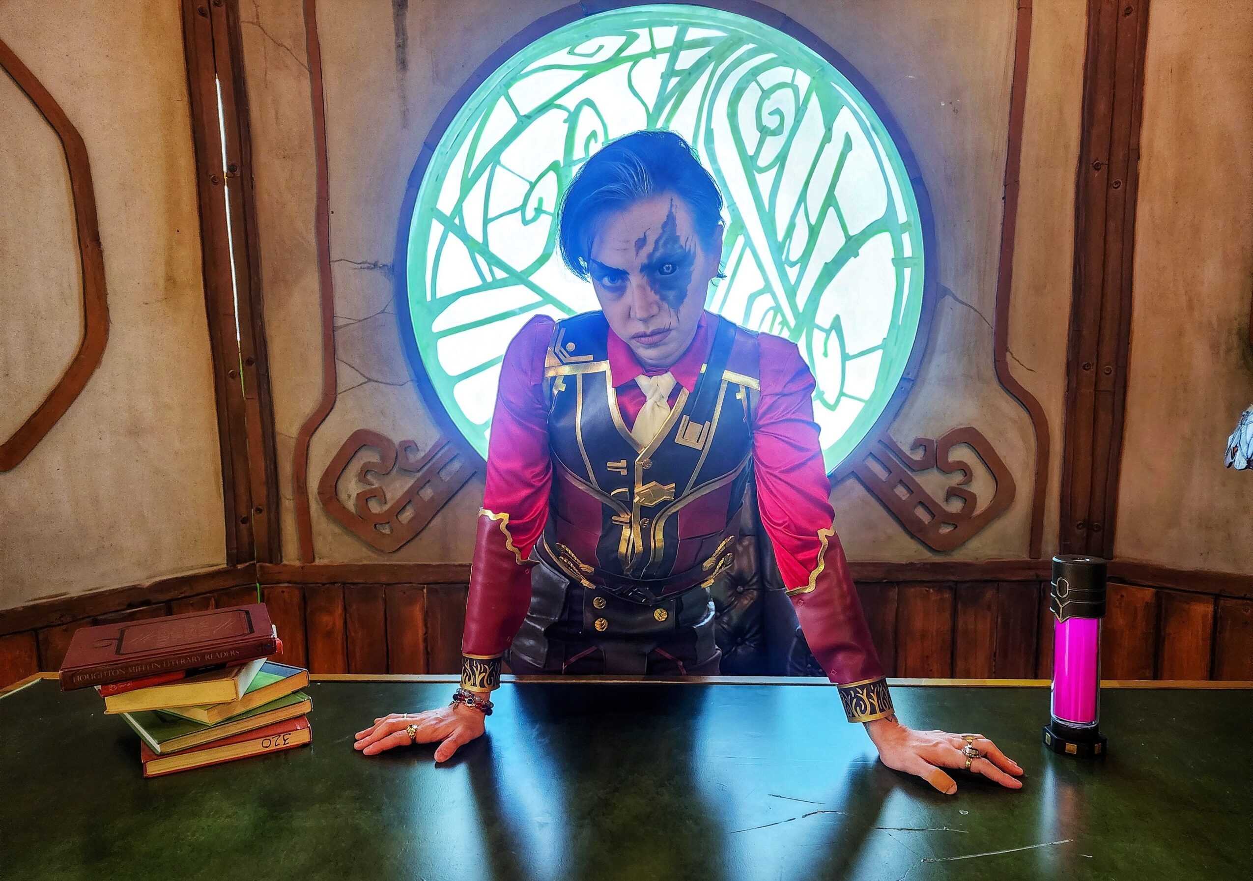 Person with sunglasses leaning over a table, with books and a pink water bottle, in a room with a circular window.