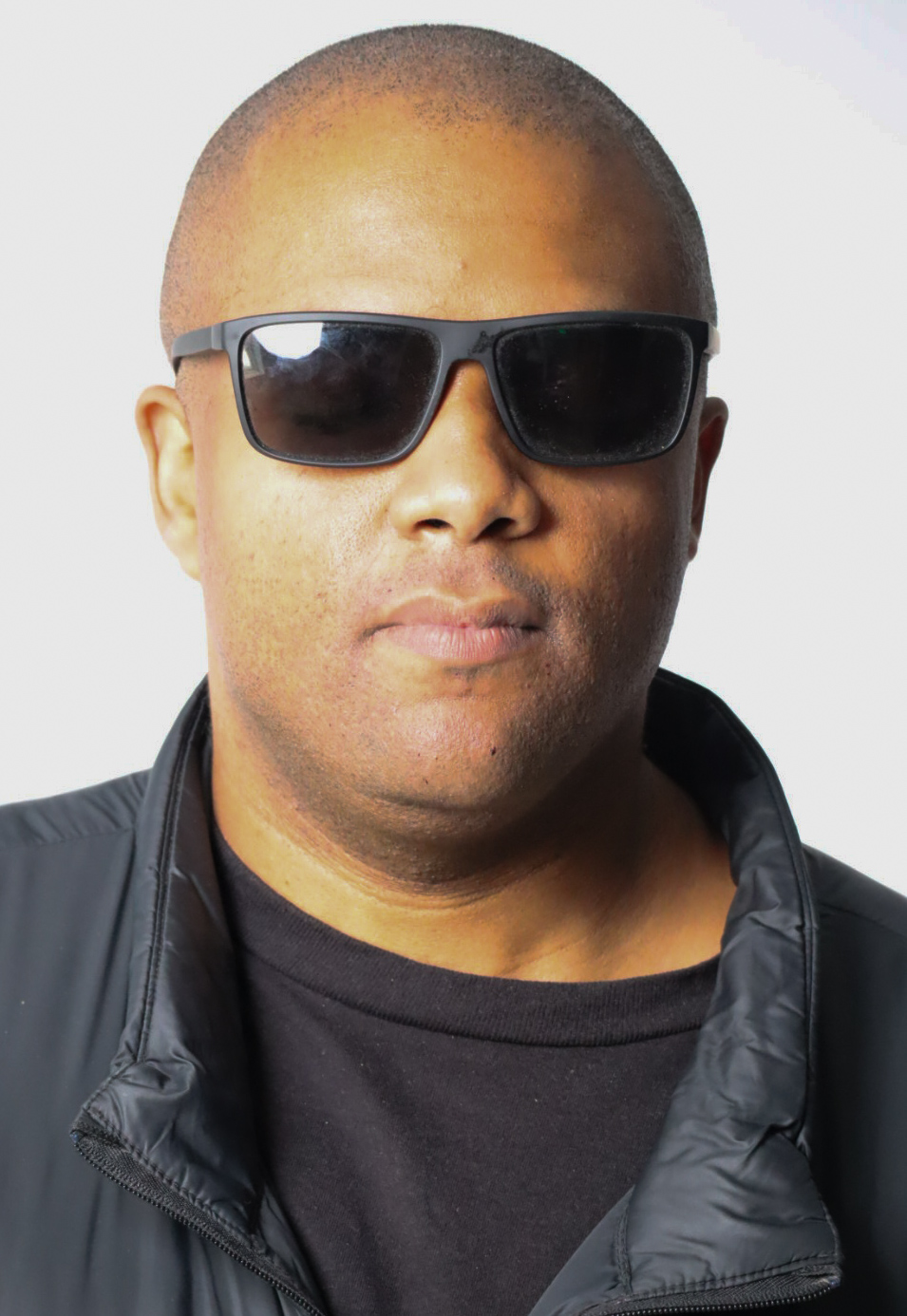 Person with short hair wearing sunglasses and a black jacket, facing forward.