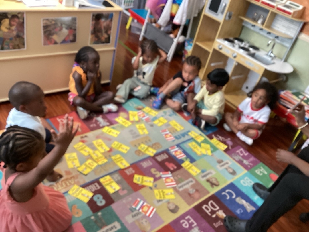 Children sit on the floor playing a card game with yellow, red, and blue cards in a classroom.