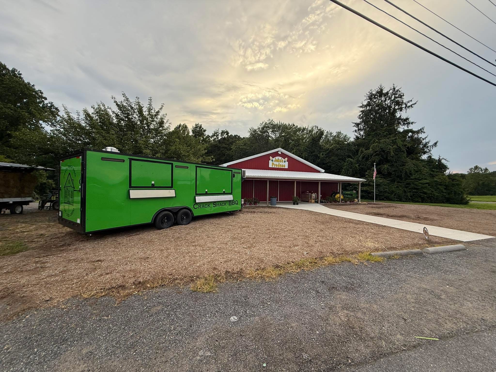 Green food truck parked in front of a red building with a white sign, trees and power lines in the background.