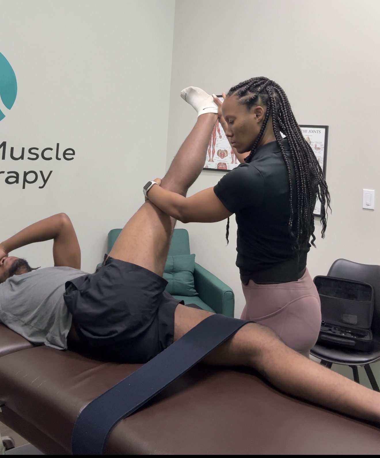 A woman receives physical therapy from a therapist, lying on a treatment table with a strap around her leg.
