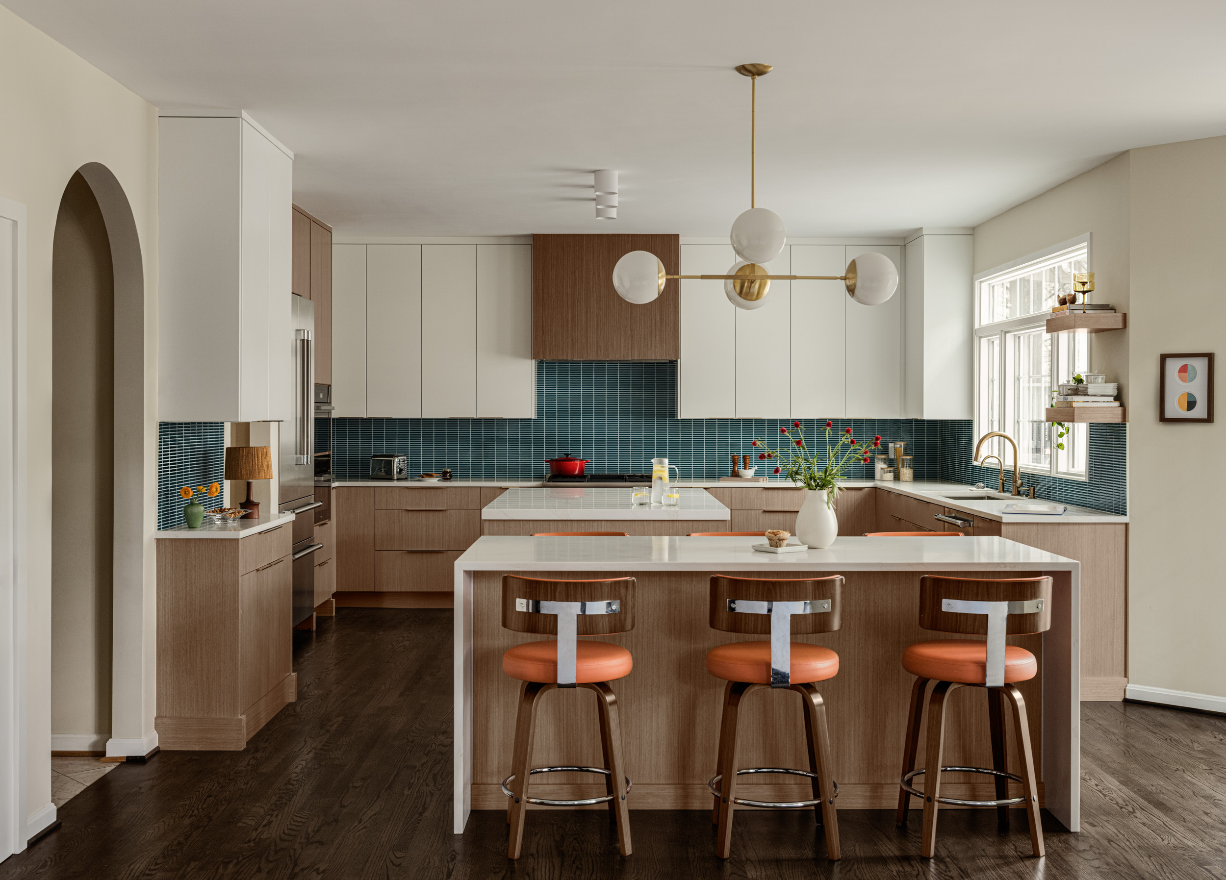 Kitchen with island, three bar stools, white cabinets, blue backsplash, and large window, bright and modern interior.