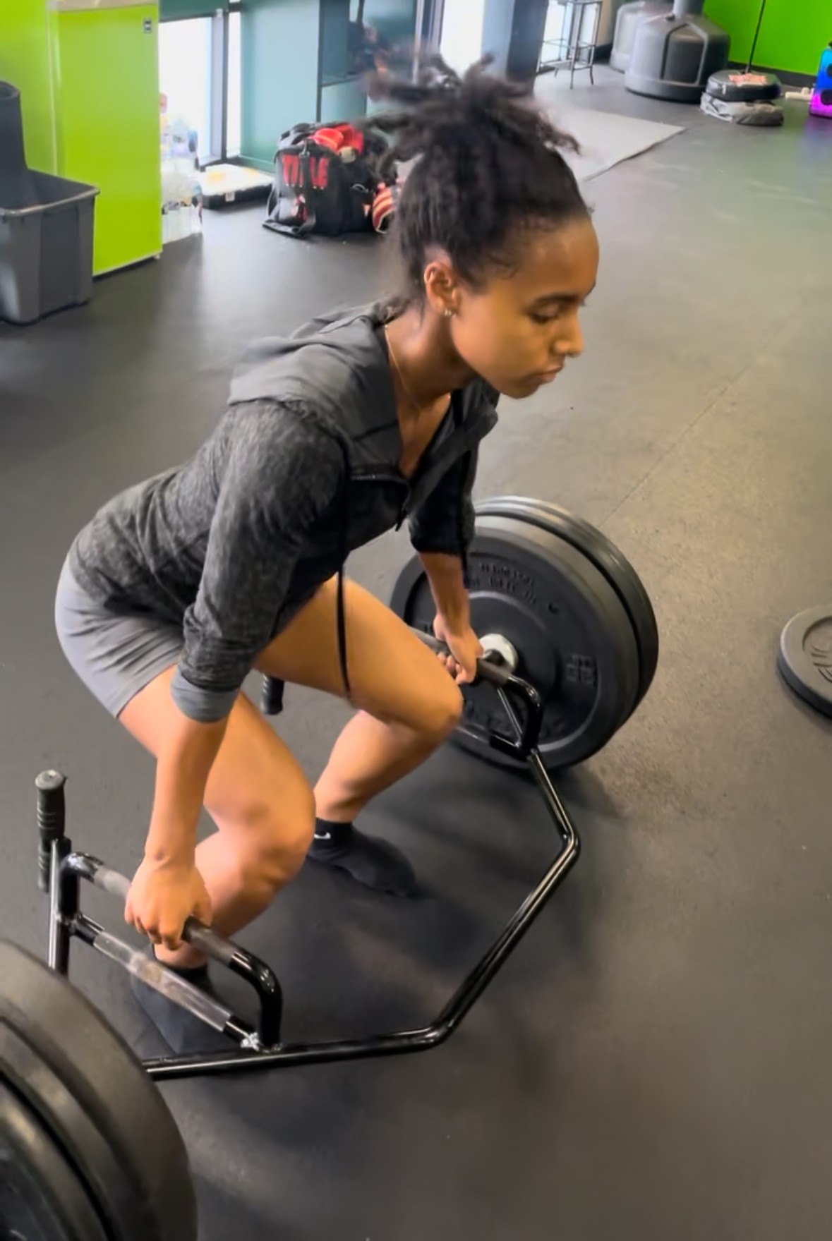 Woman in workout clothes bending over a barbell on a gym floor, preparing to lift weights.